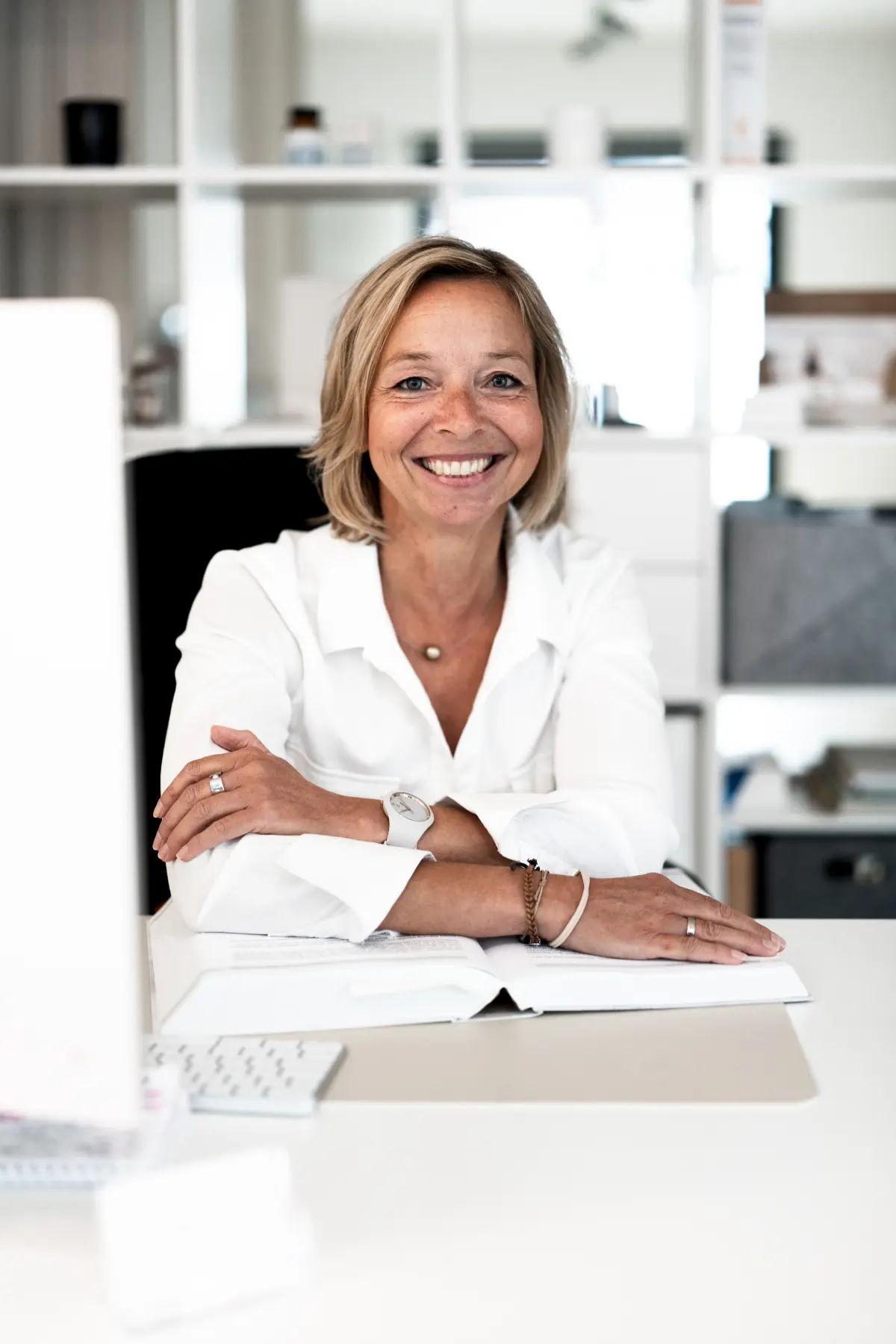 Helga sitzt am Schreibtisch und lächelt am Monitor vorbei in die Kamera