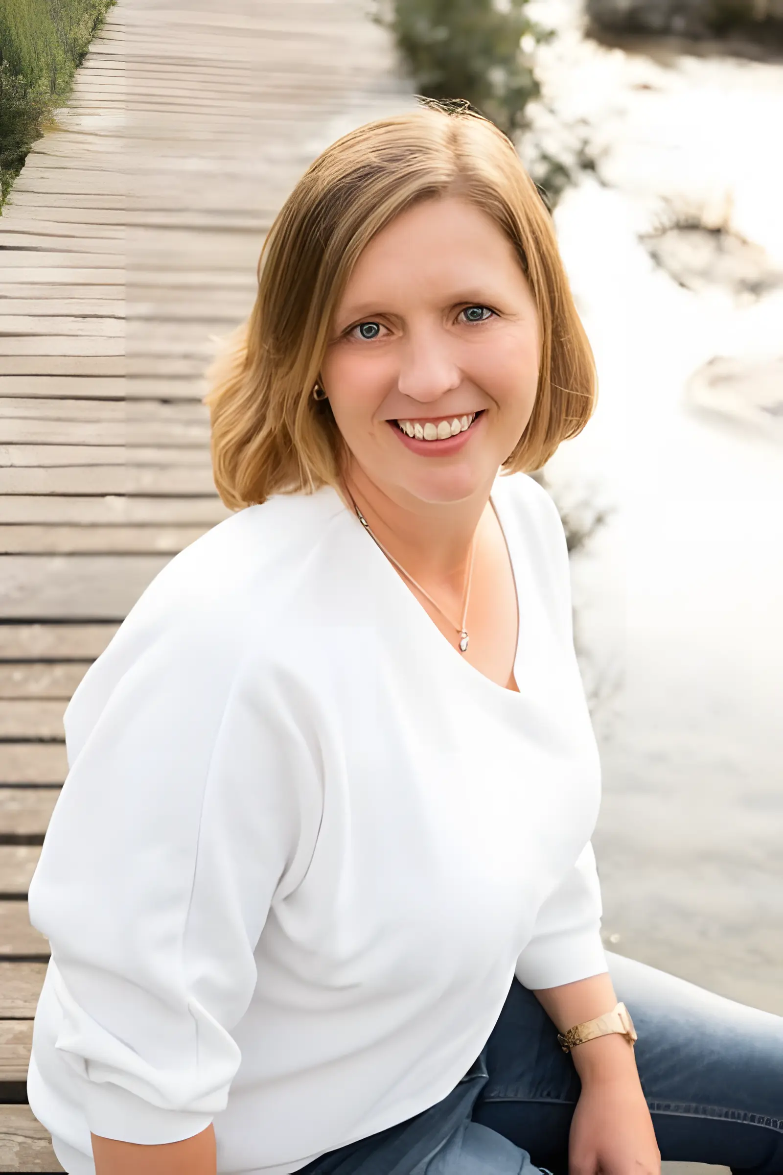 Judith Schmitz sitzt auf einem Steg am Wasser und lächelt aufwärts blickend in die Kamera